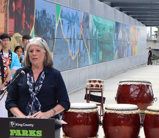 Claudia Balducci Wants to Tackle King County’s Challenges Head-On as Executive Claudia Balducci stands at a lectern with drums next to her and drummers dressed in traditional Japanese garb behind.