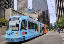 Rob Saka Pushes to Decommission the South Lake Union Streetcar A light blue streetcar tram on Westlake Avenue in South Lake Union with office buildings towering above.