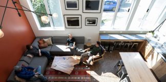 The Case for Converting Vacant Offices to Congregate Housing Four residents sit in a L couch in a lounge well-lit by natural light.