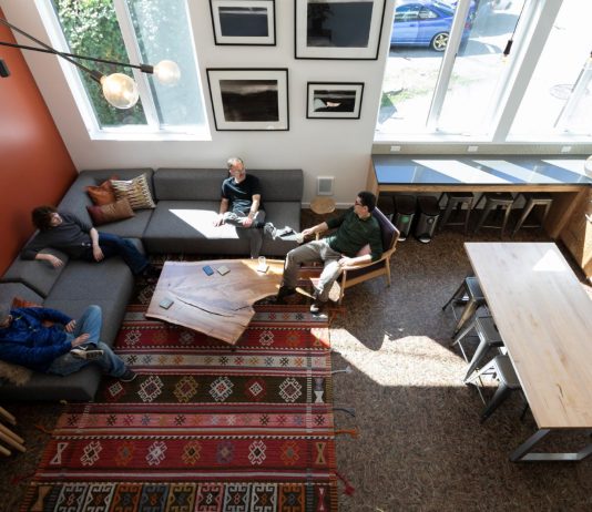 The Case for Converting Vacant Offices to Congregate Housing Four residents sit in a L couch in a lounge well-lit by natural light.