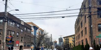Pedestrians cross Denny Way at the Harvard Avenue intersection with midrise apartment buildings in the background.