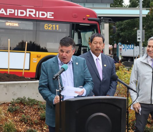 Spotts to Leave SDOT Just as New Transportation Levy Gets Rolling Greg Spotts standing at a podium with Bruce Harrell looming over and a RapidRide bus behind