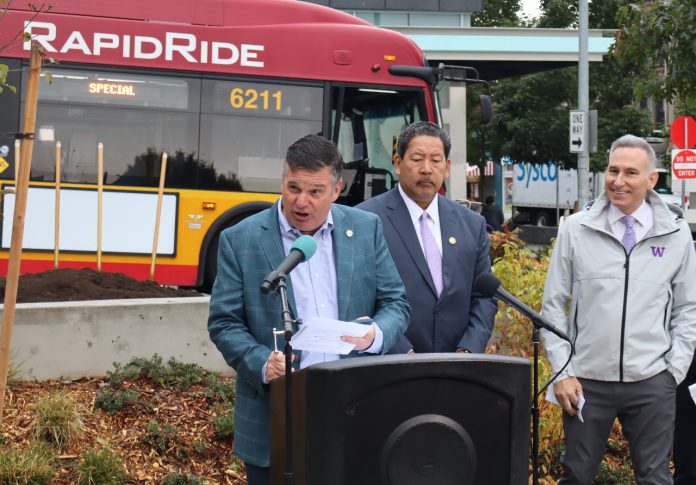 Greg Spotts Greg Spotts standing at a podium with Bruce Harrell looming over and a RapidRide bus behind