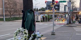 Metro Plans Reduced Service as Staff Hold Shawn Yim Memorial Friday The pedestrian bridge to the University Washington campus looms in the background and a bus stop with two buses waiting at a stop light.