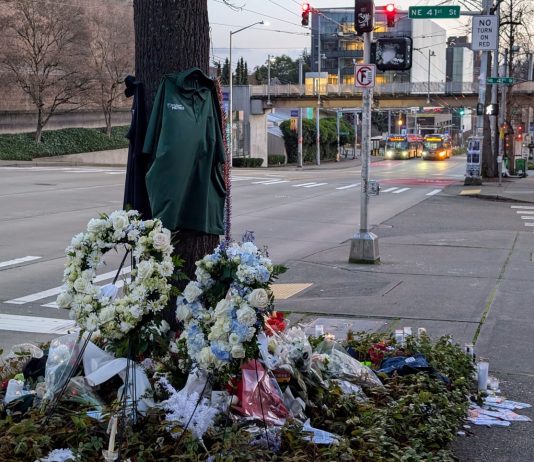 Metro Plans Reduced Service as Staff Hold Shawn Yim Memorial Friday The pedestrian bridge to the University Washington campus looms in the background and a bus stop with two buses waiting at a stop light.