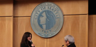 The pair stand before the Seattle city seal at Seattle City Council chambers.