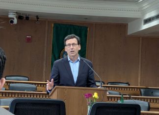 Ferguson Proposes ‘Unprecedented Sweep’ of Climate Dollars to Balance State Budget Ferguson stands at the lectern wearing a navy suit and glasses in a Capitol board room.