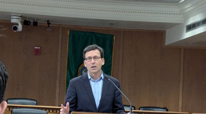 Ferguson Proposes ‘Unprecedented Sweep’ of Climate Dollars to Balance State Budget Ferguson stands at the lectern wearing a navy suit and glasses in a Capitol board room.