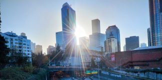 Cars use Interstate 5 through Seattle on a sunny day, with the sun just breaking through the city skyline