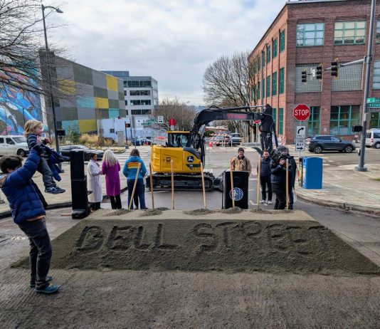 Seattle Breaks Ground on Bell Street Bike Lane, Waterfront Park Linkage Bell Street is written into the pile of sand that was used in the ceremonial groundbreaking shoveling. A man hoists his child and officials mill about after the ceremony.