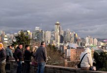 How Much Housing Growth Should Seattle Be Targeting? A handful of people stand at the railing at Kerry Park overlooking the Seattle skyline with the space needle prominently in the needle and they snap photos.