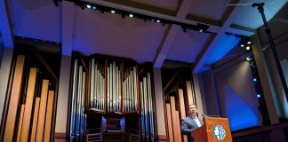 Harrell stands at a lectern with a big pipe organ behind him on the Benaroya auditorium stage.