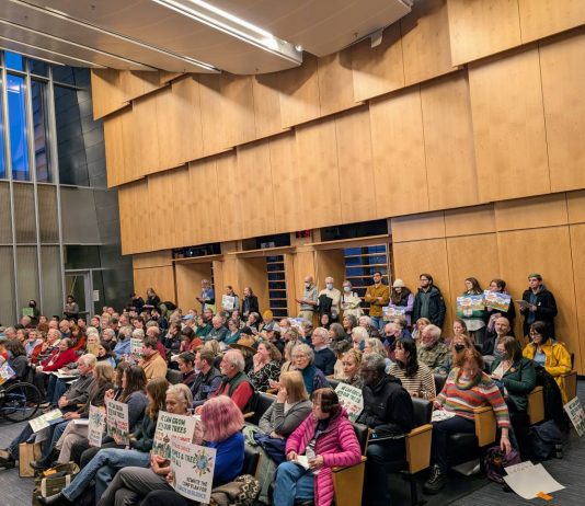 Housing Advocates Outnumber ‘One Seattle’ Opponents, Moore and Rivera Back Opponents The Seattle council chambers are filled to the brim. People hold signs to promote their views.