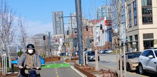 A person on a Brompton folding bike wearing a mask and biking south on Alaskan Way's bike lane near Seneca Street