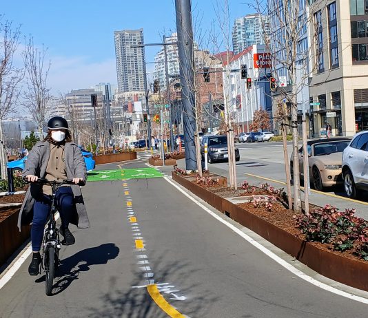 Seattle’s Waterfront Bike Path Opens After Long Wait A person on a Brompton folding bike wearing a mask and biking south on Alaskan Way's bike lane near Seneca Street