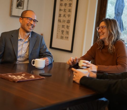 Eddie Lin Pushes Housing in Council Bid to Represent Southeast Seattle Lin is an Asian man with glasses and a suitcoat. He holds a coffee cup and sits next two people, one of them his wife.