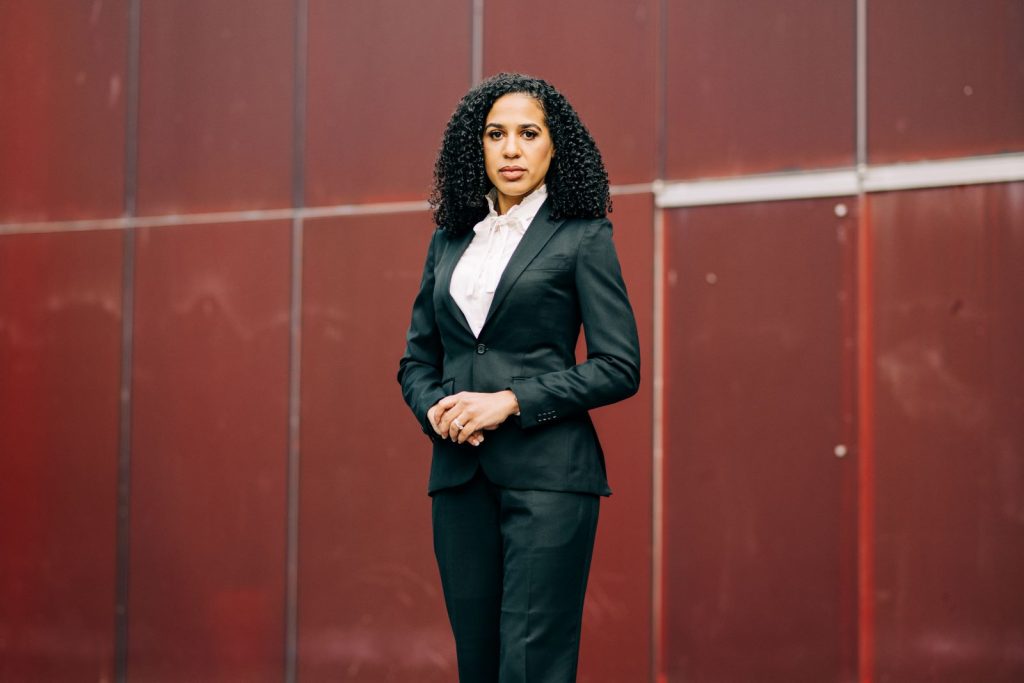 Evans is a light-skinned Black woman with curly hair standing in front of a red wall.