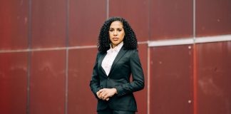 Prosecutor Erika Evans Stresses Federal Experience in Seattle City Attorney Bid Evans is a light-skinned Black woman with curly hair standing in front of a red wall.