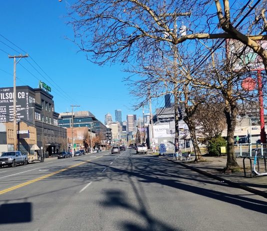 Seattle Council Lifts Ban on Housing in Stadium District The view of wide, but empty First Avenue looking north toward Downtown, with low-slung industrial, strip mall, and parking lots around it.