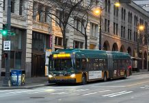 King County Council Wants Fewer ‘Ghost’ Buses and Better Data Collection A bus sports King County Metro's green and gold livery with masonry buildings in the background.