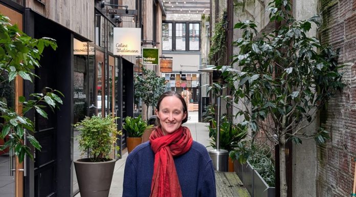 Wilson Pulls Within Two Points of Harrell in Friday Count Wilson wear a red scarf and a dark blue coast and stand in the Chophouse Row alley which is lined by potted plants and restaurant storefronts.