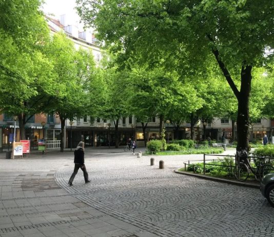 Op-Ed: Harrell’s Growth Plan Shorts Housing and Tree Canopy A quiet pedestrian street with a few people walking and plenty of tree canopy with a midrise residential building in the background.