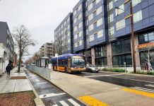 Op-Ed: Single Family Zoning Is Keeping Seattle Inaccessible to Disabled People A travels down Roosevelt Way next to the protected bike lane. A large seven-story apartment building with a crawfish restaurant on the first floor is on the right.