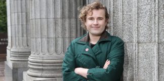 Ry Armstrong Lays Out Progressive Contrast Against Mayor Harrell Ry stands in front of a Greek column with their arms crossed