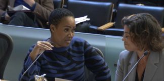 Washington is a black woman with short hair. She holds the microphone and looks to her left toward Natalie Walton-Anderson and the auditor as she delivers her rebuttal.