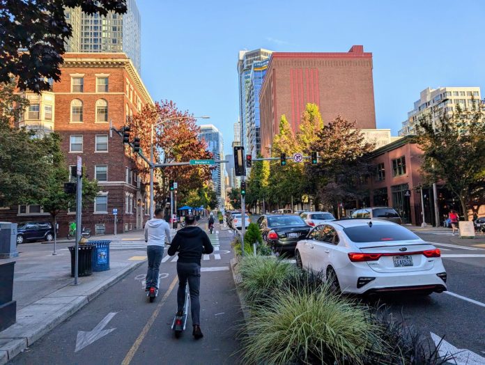 Two riders push off to accelerate on their Lime scooters on the Second Avenue protected bike lane in Belltown.