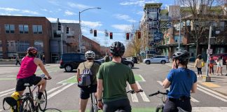 Op-Ed: Anti-Speeding Technology Could Have Saved My Son Five people on bike wait in a green bike lane at a major intersection with car whizzing by and pedestrians waiting on the corner.