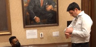 Shane Esquibel answers a call coming through on his smartwatch, as Scott sits and looks in from the Governor's waiting room, adorned with official portraits of governors long past.