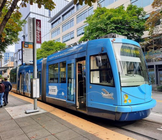 Fare Hike Proposal Would Increase Seattle Streetcar Rides to $3 A blue streetcar at a stop along Westlake Avenue with three passengers on the platform.