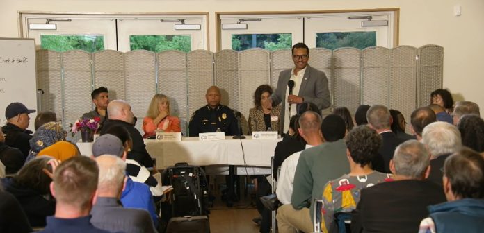 Rob Saka with D1 Town Hall Safety Panel - Seattle Channel Police Chief Shon Barnes sits at the center of the panel and Saka stand in front the table with the mic.