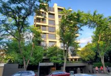 Op-Ed: Building Code Changes to Promote Better Multifamily Housing in Seattle The skinny modern eight-story towers peeks out between two trees.