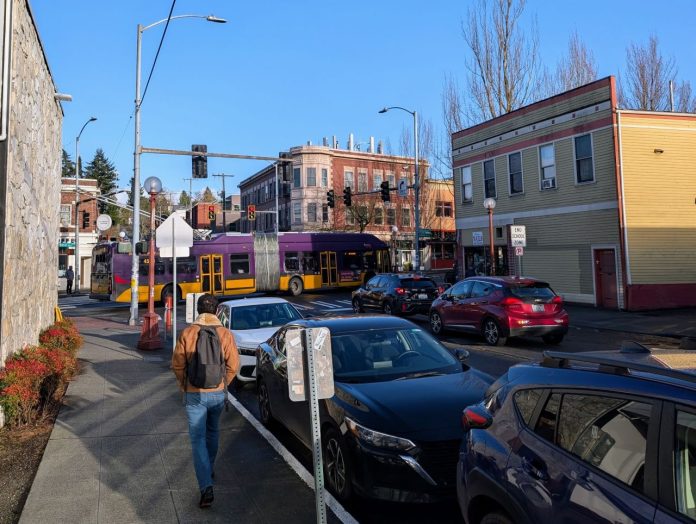 Columbia City bus and pedestrian - Urbanist 20250305 A bus on Rainier Avenue passes by as a pedestrian walks up the side street in Columbia City.