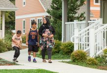 License Plate Readers Proliferate in Washington, Bringing Concerns over ICE Overreach A mother and her two sons walk on a pedestrian path between a row of townhomes. She wears a headscarf and her older son wears a Lebron James jersey. The younger is on a skateboard.