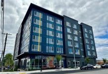 King County’s Housing First Initiative Boasts High Success Rate A blue six-story building with a bright cloudy sky in the background