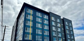 A blue six-story building with a bright cloudy sky in the background