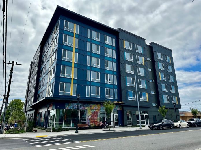 A blue six-story building with a bright cloudy sky in the background