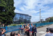 Seattle Leaders Tout Bike and Pedestrian Upgrades for Pike and Pine Harrell holds ceremonial gold scissors to cut the red ribbon on a widen sidewalk next to a new protected bike lane on Pike Street on the I-5 overpass bridge to Capitol Hill. The new convention center is in the background.