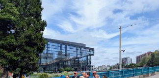 Seattle Leaders Tout Bike and Pedestrian Upgrades for Pike and Pine Harrell holds ceremonial gold scissors to cut the red ribbon on a widen sidewalk next to a new protected bike lane on Pike Street on the I-5 overpass bridge to Capitol Hill. The new convention center is in the background.