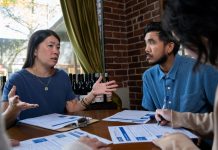 Jeanie Chunn Wants to Reverse D2’s Neglect in Seattle Council Bid An Asian woman with straight long black hair, Chunn sits at a table gesturing broadly with hands talking to the man seated next to her.