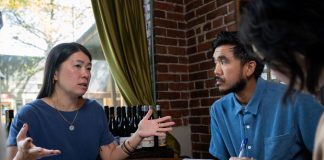 Jeanie Chunn Wants to Reverse D2’s Neglect in Seattle Council Bid An Asian woman with straight long black hair, Chunn sits at a table gesturing broadly with hands talking to the man seated next to her.