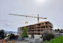 Harrell Proposes Design Review Moratorium, Interim Legislation Complying with State Mandate The mass timber framework is visible on a six-story office building as a tower crane lowers a siding panel into place.