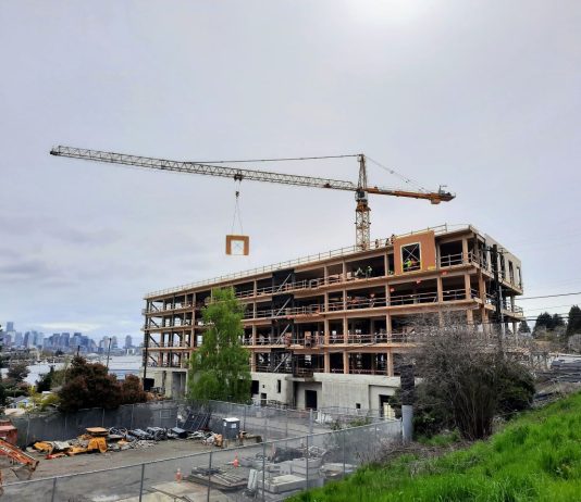 Harrell Proposes Design Review Moratorium, Interim Legislation Complying with State Mandate The mass timber framework is visible on a six-story office building as a tower crane lowers a siding panel into place.