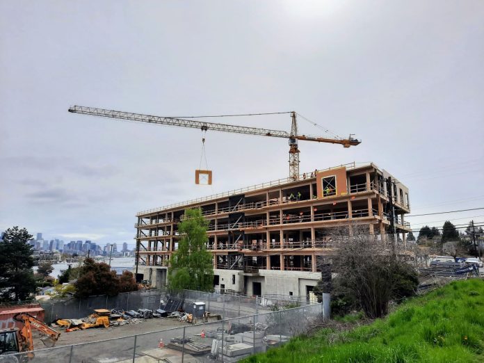 Mass timber building Wallingford Lake Union - Trumm 20230421 The mass timber framework is visible on a six-story office building as a tower crane lowers a siding panel into place.