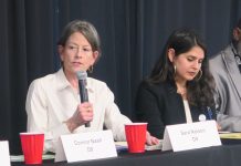Seattle Council Candidates Spar at Mobility and Housing Forum Sara Nelson holds a microphone and wears a white button-up shirts. She sits a long table next to Alexis Rinck, who wears a black blazer and hoop earrings.