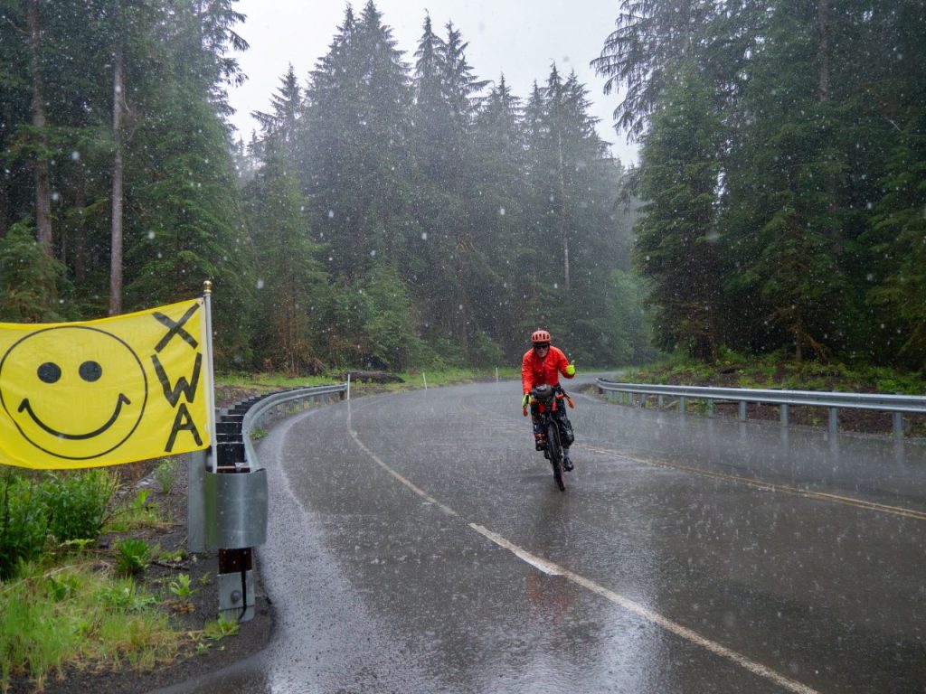 A yellow XWA sign with the smile-y face symbol adorns a traffic railing on a mountain road