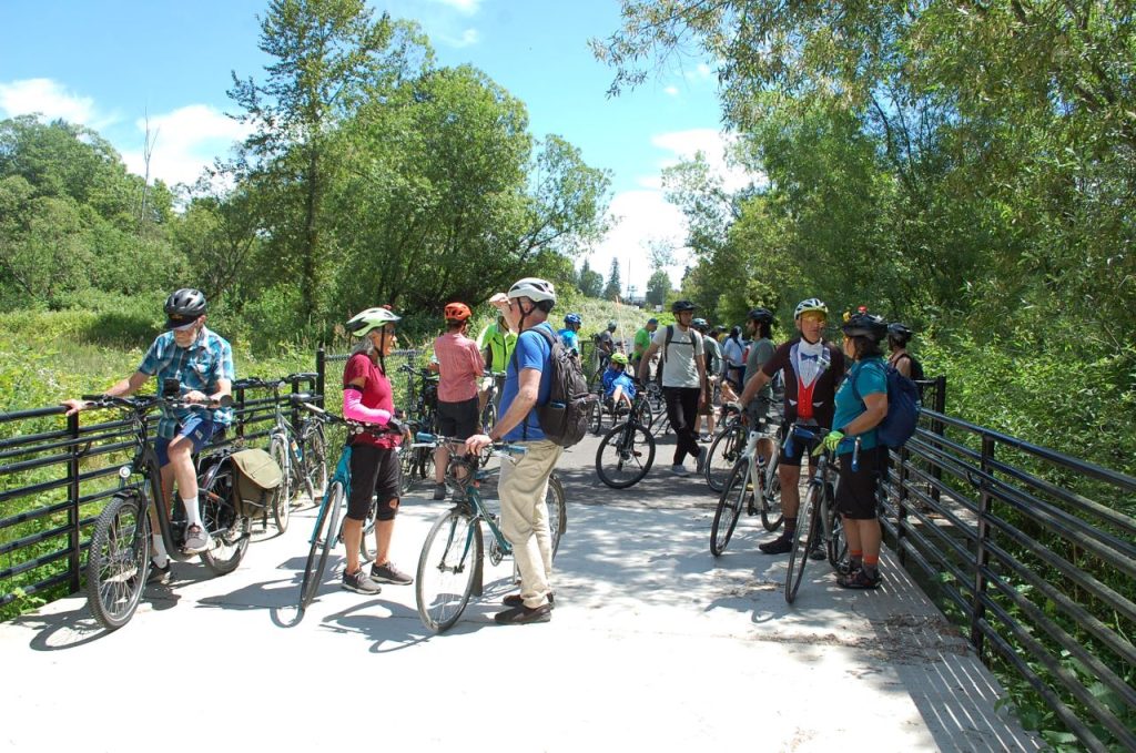 A group of over dozen people with their bikes on a wetland boardwalk segment of the trail.
